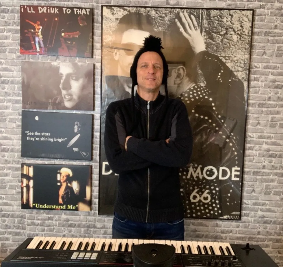 Scott, founder of Diary of a Devotee, wearing a Martin Gore mohawk hat in front of his Depeche Mode wall and keyboard.